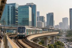 Rapid Metro train with teal doors on an elevated viaduct past DLF Cyber City glass towers in Gurgaon